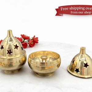 May include: Three brass incense burners. One burner has a lid with star-shaped cutouts. The other two are open bowls. Red flowers are in the background. The burners are on a white marble surface.