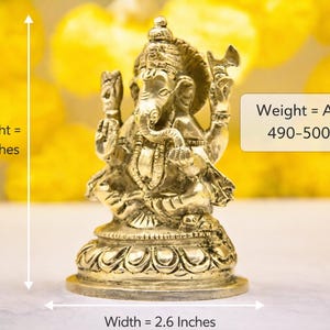 Puede incluir: Estatua dorada de Ganesha, deidad hind&uacute;, sentado sobre una base de loto. La estatua mide 10 cm de alto y 6,6 cm de ancho. El peso es de aprox. 490-500 gramos. El fondo est&aacute; borroso con tonos amarillos.