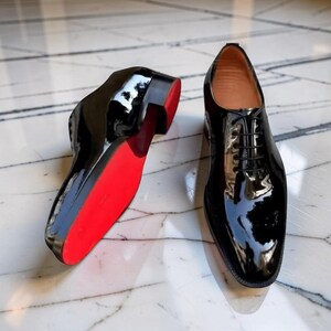 以下が含まれることがあります： 赤いソールが特徴的な、光沢のある黒い革のドレスシューズのペア。靴はクラシックなレースアップデザインで、光を反射するハイシャイン仕上げです。赤いソールが黒いアッパーと対照的です。