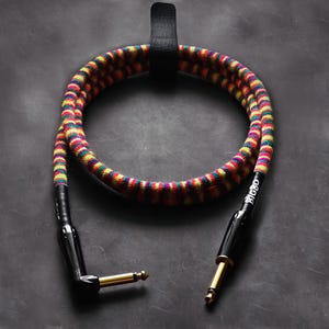 Pode incluir: Um cabo de guitarra listrado colorido com conectores pretos e a palavra "RIGIDO" impressa no cabo.