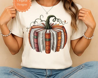 May include: Cream-colored t-shirt featuring a pumpkin design made of books. The pumpkin has a green stem and is surrounded by open books with orange, red, and brown spines. The text "Original Designs" is in a circular orange shape in the upper left.