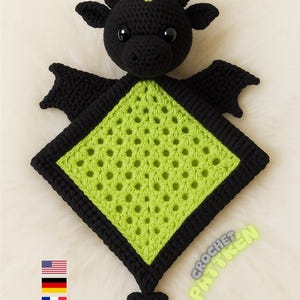 May include: A handmade crochet dragon toy in black and green. The dragon has a black head with small ears and a green crest. The body is a green square with a black border and wings. The text "booktunnel" is at the top.
