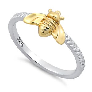 May include: A silver ring with a textured band and a gold bee charm. The ring is stamped with "925" on the inside.