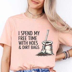 Puede incluir: Camiseta de color melocotón claro con el texto "I SPEND MY FREE TIME WITH HOES & DIRT BAGS" en negro. Un gráfico de una pala y una bolsa de tierra está impreso en la camiseta. La camiseta está hecha de un material suave.