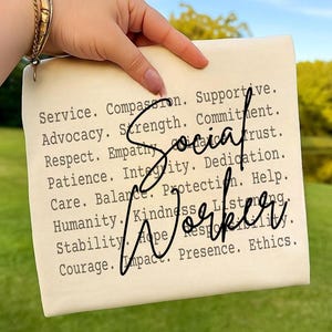 May include: A cream-colored rectangular sign with the words "Social Worker" in a handwritten font. The sign lists words like "Service," "Compassion," and "Advocacy" in a typewriter font. A gold bracelet is visible.