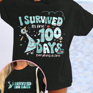 May include: Black t-shirt featuring the text "I Survived 100 Days" in blue and white. The design includes a cartoon pigeon, apple, and pencils. The phrase "Everything is fine" is also printed on the shirt.