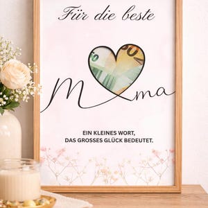 May include: A framed print with the words "Für die beste Mama" and "Ein kleines Wort, das grosses Glück bedeutet." A heart shape contains a Euro bill. The print is in a light wood frame.