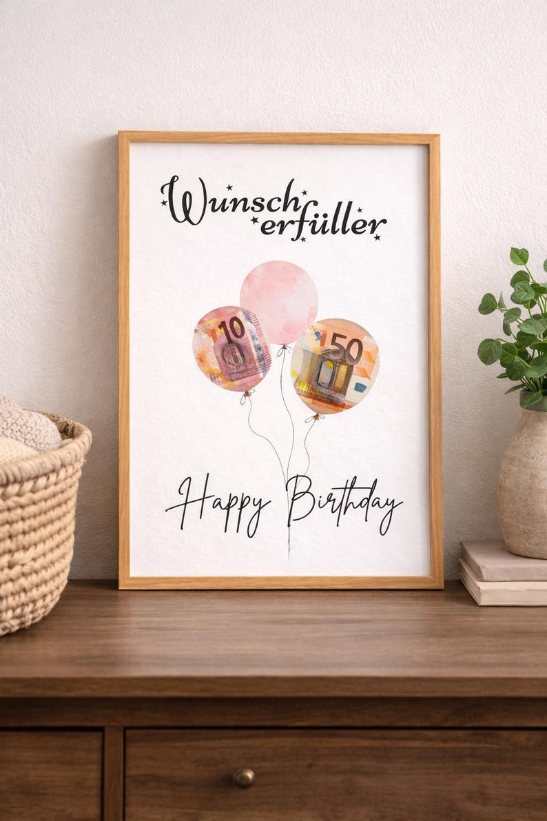 May include: A framed print with a light wood frame. The artwork features three balloons, two with currency designs and one pink. The text "Wunscherf&uuml;ller" and "Happy Birthday" are written in black script.