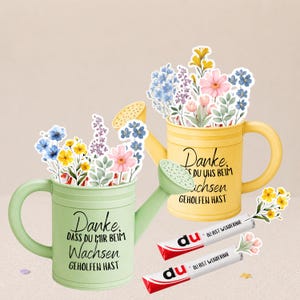 May include: Two watering cans, one green and one yellow, filled with paper flowers. The green can has the text "Danke, dass du mir beim Wachsen geholfen hast." The yellow can has the text "Danke, du uns beim Wachsen geholfen hast."