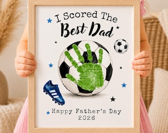 Könnte beinhalten: Ein gerahmter Druck mit einem Fußball, einem grünen Handabdruck in der Mitte, einem blauen Fußballschuh und dem Text I Scored The Best Dad Happy Father's Day 2026, verziert mit kleinen blauen und schwarzen Sternen auf weißem Grund.