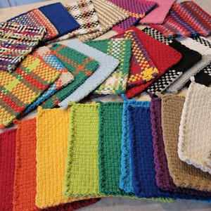 May include: A collection of colorful, woven potholders in various patterns and hues. The potholders are arranged in a visually appealing display, showcasing a range of colors from red and orange to green, blue, and purple. Some have loops for hanging.