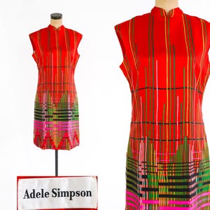 Op de afbeelding: Een rode, mouwloze jurk met een geometrisch patroon in zwart, groen, roze en geel. De jurk heeft een mandarijnsluiting en is gelabeld "Adele Simpson".