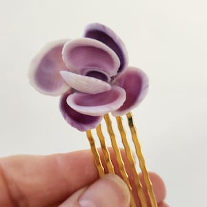 May include: A purple seashell flower hair comb with a gold metal comb. The comb has five tines.