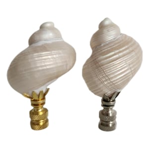 Może przedstawiać: Dwa białe zakończenia do lamp z muszli z podstawami w kolorze złotym i srebrnym. Muszle są opalizujące i mają spiralny kształt.