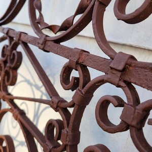 Pu&ograve; includere: Primo piano di una sezione di una recinzione decorativa in ferro battuto. La recinzione &egrave; verniciata di un marrone scuro e presenta intricate volute e disegni curvi. La recinzione sembra invecchiata, con alcuni segni di ruggine.