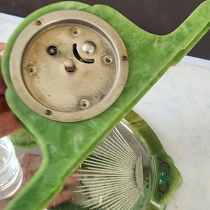 May include: A vintage vanity set in green, including a hand mirror and a small tray. The mirror has a silver face and a green handle. The tray features a sunburst design, with a green border.