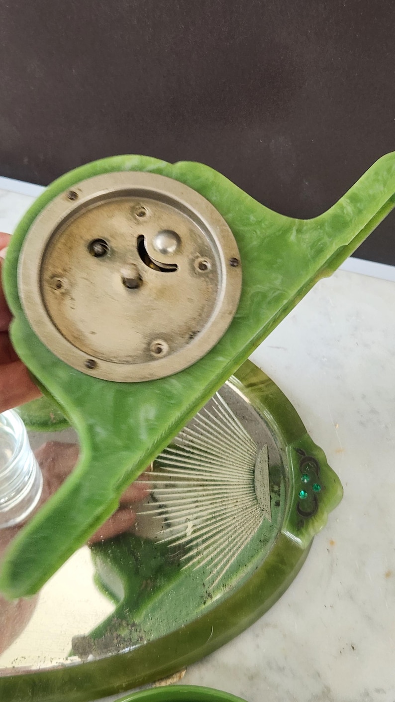May include: A vintage vanity set in green, including a hand mirror and a small tray. The mirror has a silver face and a green handle. The tray features a sunburst design, with a green border.