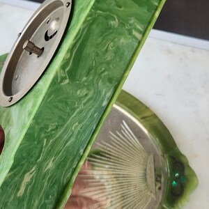 May include: Vintage green and white marbled vanity tray with a silver-toned metal accent. The tray has a decorative shape with a matching hand mirror. The mirror has a silver-toned metal back and a decorative design.
