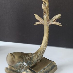 May include: A vintage brass sculpture of a mythical creature, possibly a dragon or sea serpent. The sculpture has a square base, a curved body, and a detailed head. The top features a decorative element.