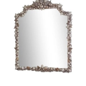 May include: A rectangular mirror with a decorative frame made of various seashells. The frame is a mix of white, beige, and black shells, creating a textured border around the reflective glass. The mirror has a unique, arched top.