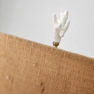 May include: White coral finial with a gold base, sitting on a brown burlap surface.
