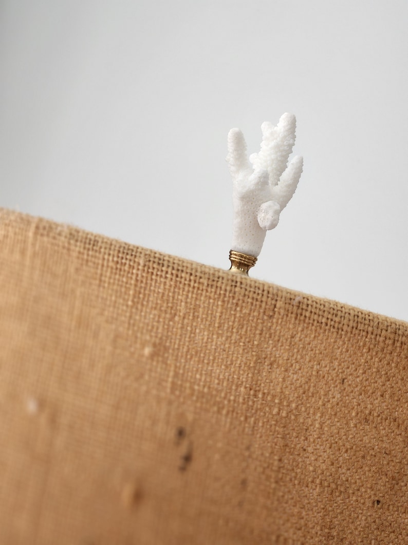 May include: White coral finial with a gold base, sitting on a brown burlap surface.