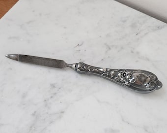 May include: A silver nail file with an ornate floral design on the handle.