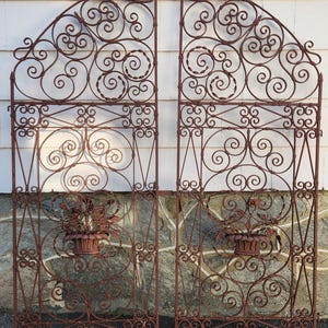 Pu&ograve; includere: Due cancelli ornamentali in ferro battuto color ruggine. Ogni cancello presenta un'intricata lavorazione a volute, accenti floreali e una fioriera decorativa. I cancelli sono progettati con un telaio rettangolare e una parte superiore ad arco, adatti per un giardino o un ingresso.