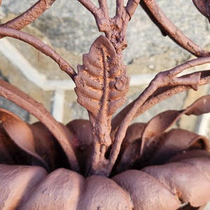 Pu&ograve; includere: Primo piano di un motivo floreale decorativo in metallo marrone arrugginito. L'immagine mostra foglie e petali dettagliati, con un aspetto strutturato e invecchiato. Il design sembra far parte di una struttura pi&ugrave; grande, forse un cancello o un elemento da giardino.