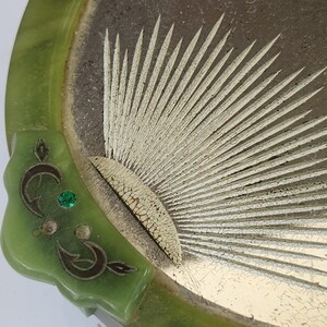 May include: A vintage green jade-coloured tray with a decorative design. The tray features a sunburst pattern in the centre with a gold-coloured finish. The rim is a darker green, and there is a decorative corner with a green gem.