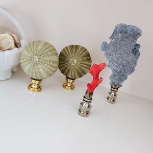 Puede incluir: Un conjunto de remates de lámpara decorativos con temática marina. Incluye dos remates de erizo de mar con bases de latón, un remate de coral rojo y un remate de coral azul. Estos remates únicos añaden un toque costero.