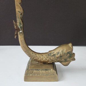 May include: A vintage brass sculpture of a fish with a curved body and a square base. The fish has detailed scales and fins, with a weathered, aged appearance. The sculpture is a decorative item.