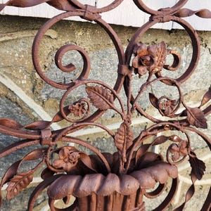 Pu&ograve; includere: Primo piano di una sezione di cancello decorativo in ferro battuto marrone arrugginito. Il design presenta elementi floreali, tra cui fiori e foglie, e accenti a spirale. Il cancello &egrave; probabilmente per uso esterno.