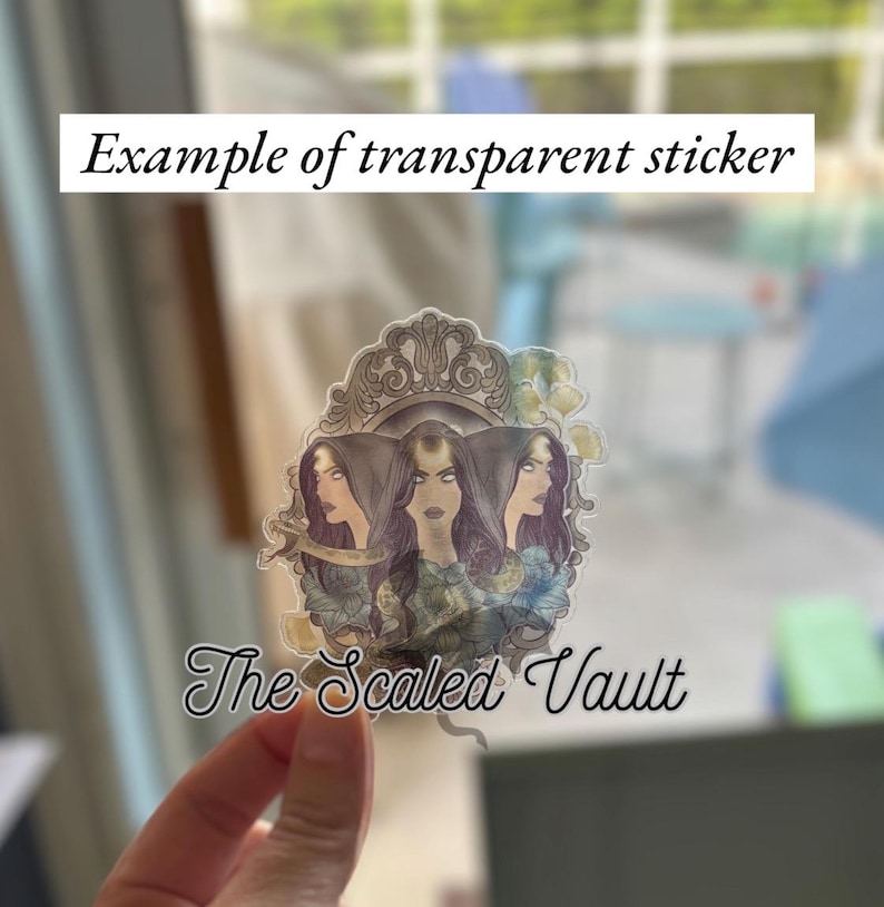 Peut inclure: Autocollant transparent repr&eacute;sentant trois figures f&eacute;minines stylis&eacute;es aux cheveux fonc&eacute;s et aux expressions intenses, encadr&eacute;es par une bordure orn&eacute;e. Le texte "Example of transparent sticker" et "The Scaled Vault" est inclus.