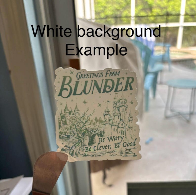 Peut inclure: Un autocollant avec un design fantaisiste avec le texte "Greetings From Blunder" en vert d'eau. L'illustration comprend un ch&acirc;teau, des arbres et les phrases "Be Wary, Be Clever, Be Good". L'autocollant a un fond blanc.