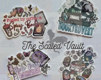 May include: Four stickers with book-themed designs. One sticker says "Fueled by coffee Spicy Books" with a coffee cup, chili peppers, and a book. Another says "Booktrovert" with a raccoon on books. The third says "Slow Burn Enthusiast" with candles and butterflies. The last one has tea bags.