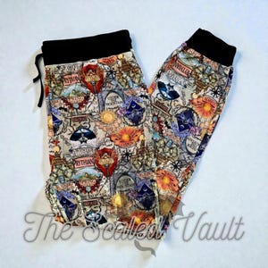 May include: A pair of patterned pants with a black waistband and drawstring. The pants feature a map-like design with various symbols, text, and colorful elements, including the words "PRYTHIAN" and "DAWN". The text "The Scaled Vault" is visible.