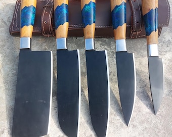 May include: Set of five black kitchen knives with wooden handles and blue resin accents. The knives are in a brown leather sheath.