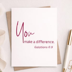 Könnte beinhalten: Eine weiße Grußkarte mit den Worten "You make a difference" in burgunderfarbener Schrift. Die Karte befindet sich auf einem braunen Umschlag, mit dem Bibelvers Galater 6:9 darunter. Ein goldener und weißer Stift ist im Hintergrund.