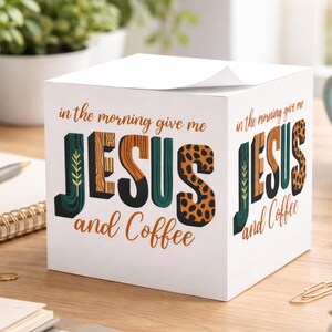 Könnte beinhalten: Ein weißer, würfelförmiger Notizblock mit dem Text "in the morning give me JESUS and Coffee". Das Wort JESUS ist in Grün, Braun und Leopardenmuster gehalten. Der Notizblock liegt auf einem Holztisch.