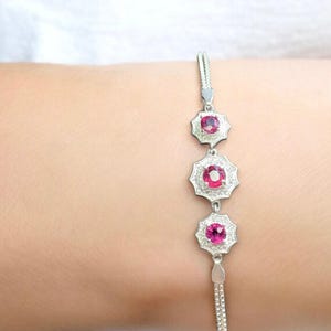 Peut inclure: Un bracelet en argent orné de trois pendentifs en forme d'étoile, chacun avec une pierre précieuse rose vif au centre, entourée de petites pierres claires. Le bracelet est délicat et élégant, avec une fine chaîne.