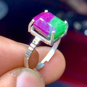 Könnte beinhalten: Ein silberner Ring mit einem grünen und rosafarbenen Edelstein. Der Edelstein ist in einer quadratischen Fassung gefasst.