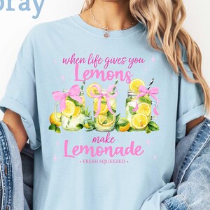 May include: A light blue t-shirt with a graphic of three mason jars filled with lemons and the text "When life gives you lemons, make lemonade. Fresh squeezed."