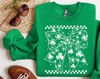 May include: Green sweatshirt with a white shamrock bow design. The bow is made up of shamrocks and has a checkered border.