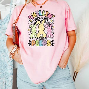 May include: Pink t-shirt with a graphic of three pastel colored bunnies with the text "Chillin' with my peeps" in rainbow colors.