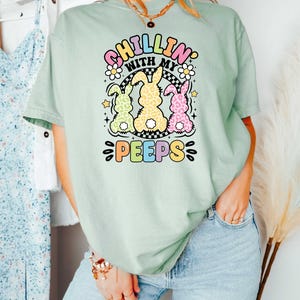May include: A light green t-shirt with a graphic of three pastel colored bunnies with the text "Chillin' with my peeps" in a rainbow font.