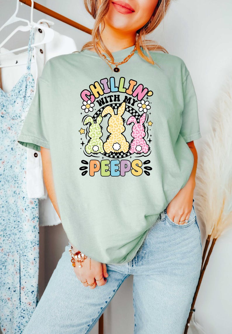 May include: A light green t-shirt with a graphic of three pastel colored bunnies with the text "Chillin' with my peeps" in a rainbow font.