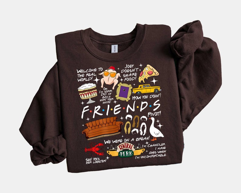 May include: A dark brown sweatshirt featuring various illustrations and text from the TV show "Friends." The design includes a turkey with a hat, a yellow taxi, a couch, and the Central Perk logo. Text includes "Welcome to the real world!" and "How you doin?"