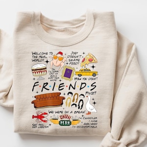 May include: Beige Friends-themed sweatshirt with various graphic elements. Features the show's logo and iconic imagery like a turkey with sunglasses, a yellow taxi, and the Central Perk logo. Text includes phrases from the show.