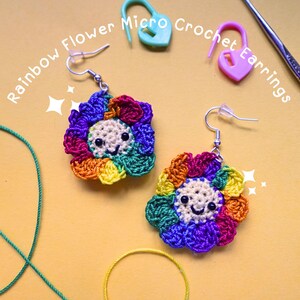 May include: Rainbow crochet flower earrings with a smiley face. The earrings are made with a variety of colors, including red, orange, yellow, green, blue, and purple.